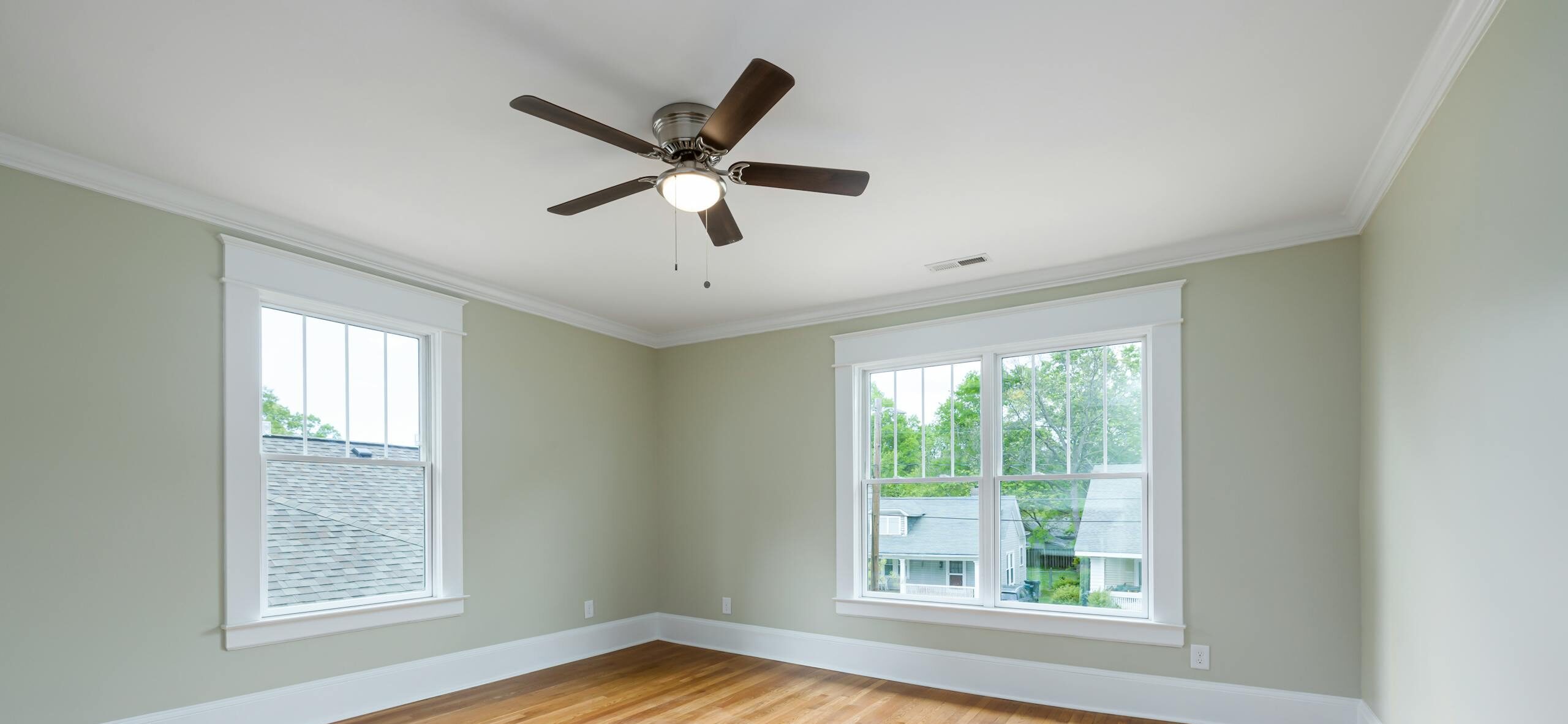Bright empty room with wooden floors, large windows, and a ceiling fan.